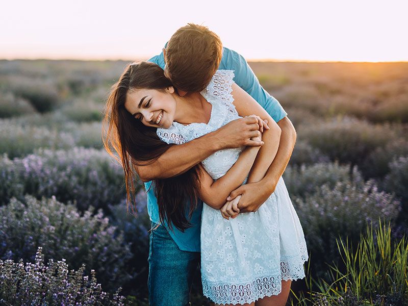 Una mujer que aprendió estos consejos de citas para mujeres de hombres abrazando a su novio y riendo en un campo de flores.