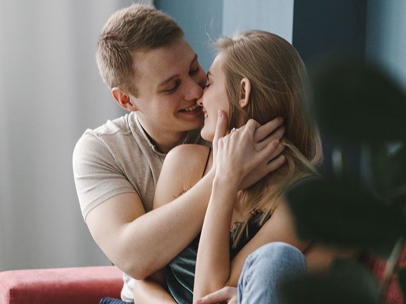 Un novio pegajoso abrazando fuerte a su novia mientras ambos sonríen y se inclinan para darle un beso.