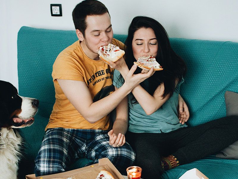 Парень, который научился флиртовать с девушкой, кормит девушку пиццей, пока она смеется и откусывает.