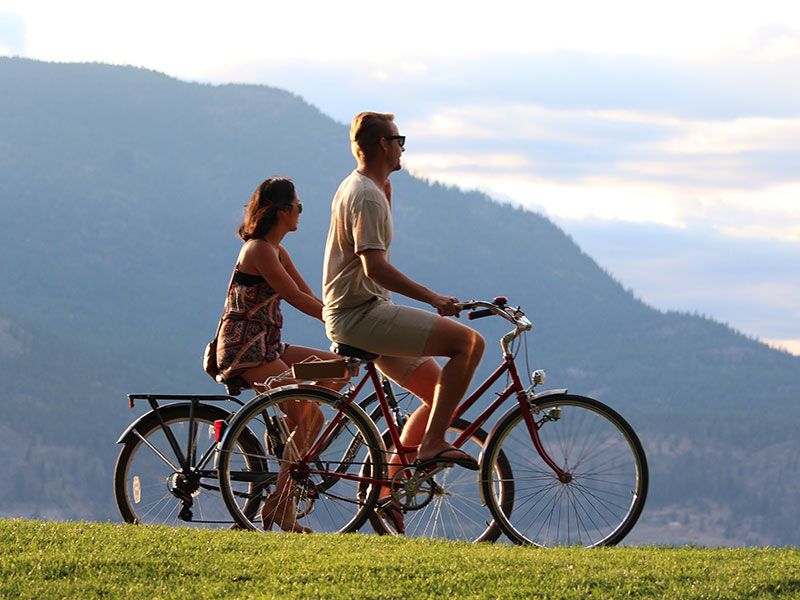 Пара катается на велосипедах на четвертом свидании, смеется и разговаривает, глядя на пейзаж.