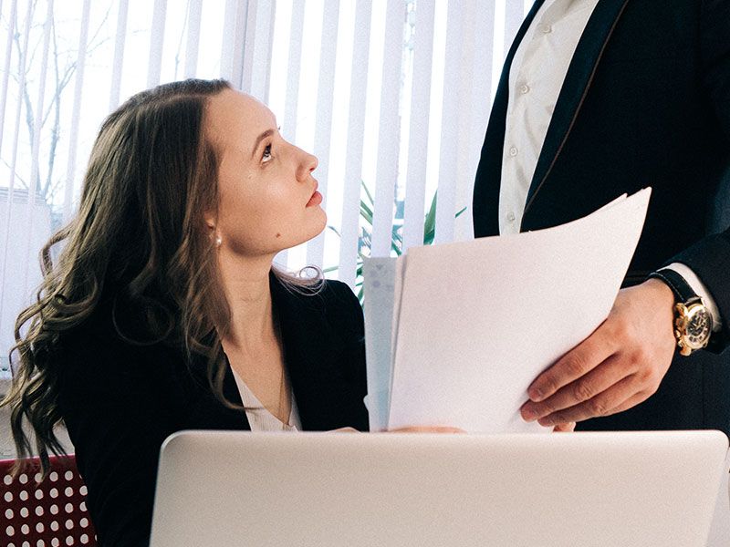 Uma mulher procurando sinais de que seu colega de trabalho casado está flertando, olhando para seu colega de trabalho enquanto ele lhe entrega um papel.
