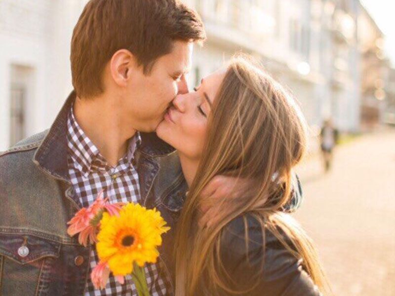 Um cara que aprendeu a cortejar alguém, beijando sua namorada enquanto segurava flores.