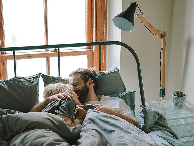 Um casal usando uma dessas maneiras de dizer aspas de bom dia e bom dia enquanto está se beijando na cama.