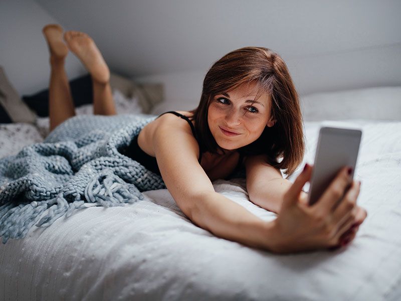 Uma mulher na cama tirando uma foto de si mesma para enviar junto com um pedido de boa noite.