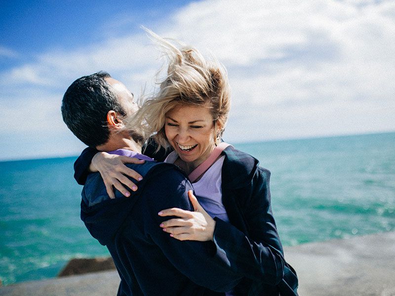 Um casal que aprendeu essas formas de demonstrar amor e carinho rindo e se abraçando na praia.