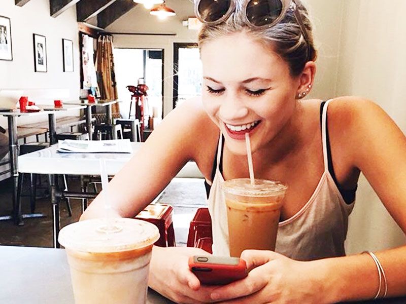 Uma mulher que aprendeu a usar o Tinder, em uma cafeteria, rindo enquanto dá um soco em caras.
